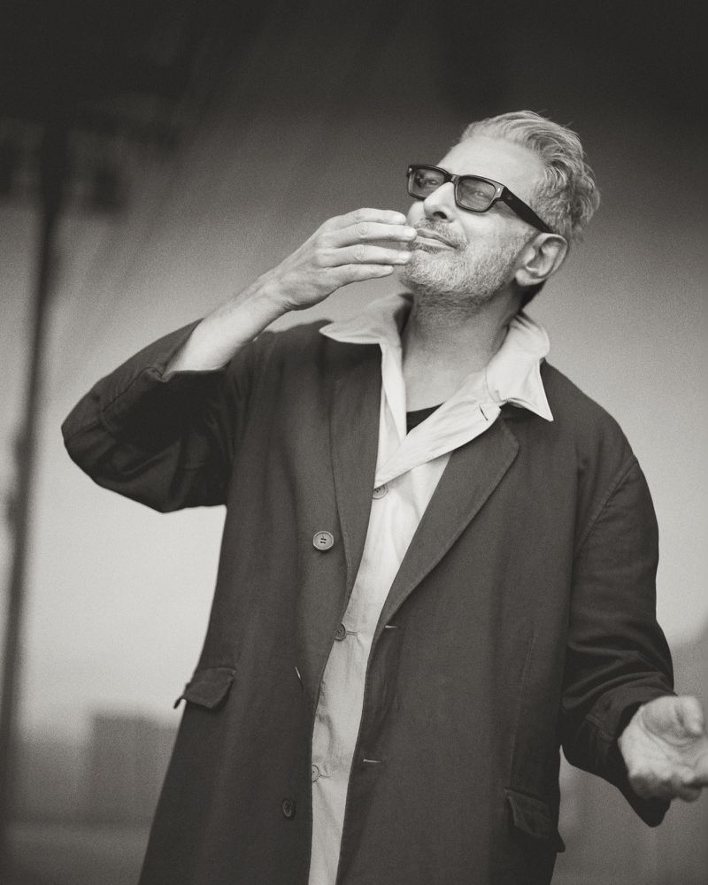 Monochrome portrait of a mature adult male with eyeglasses, wearing an open coat, holding his hand near his mouth.