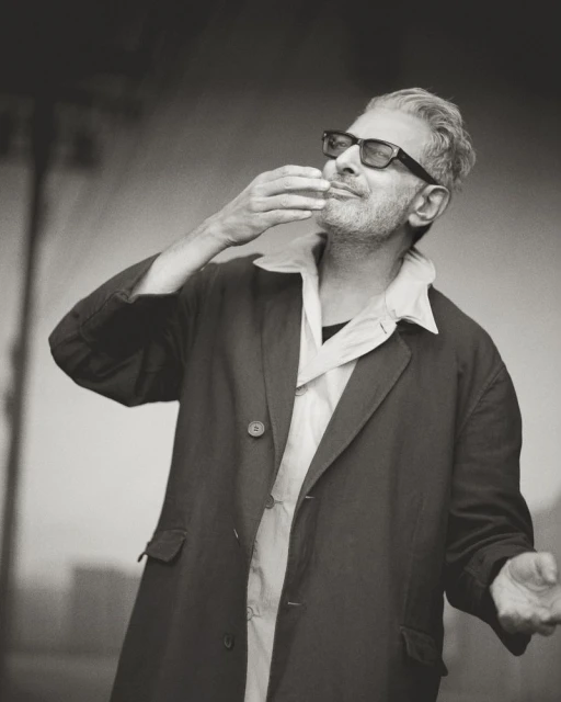 Monochrome portrait of a mature adult male with eyeglasses, wearing an open coat, holding his hand near his mouth.