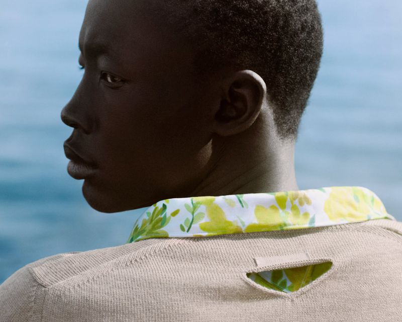 Profile of an African-American man in a tan sweater with a green floral collar against a light blue background. Fashion photography.