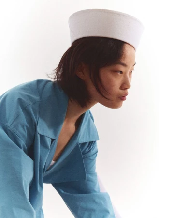 Portrait of an asian adult female wearing a sailor hat and a light blue oversized shirt on a white background in a photo studio.