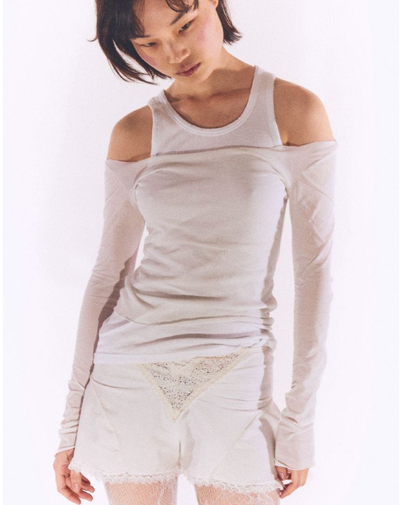 Young woman poses in a white scoop neck tank top and matching shorts with lace trim against a bright white backdrop in a fashion shot.