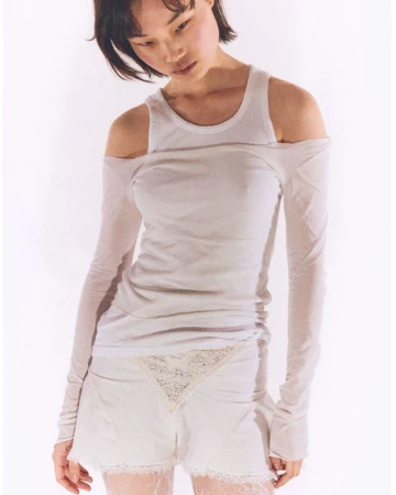 Young woman poses in a white scoop neck tank top and matching shorts with lace trim against a bright white backdrop in a fashion shot.