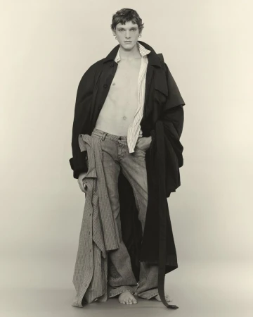 Model in dark coat and open striped shirt standing against plain background for U Repubblica project Ensemble