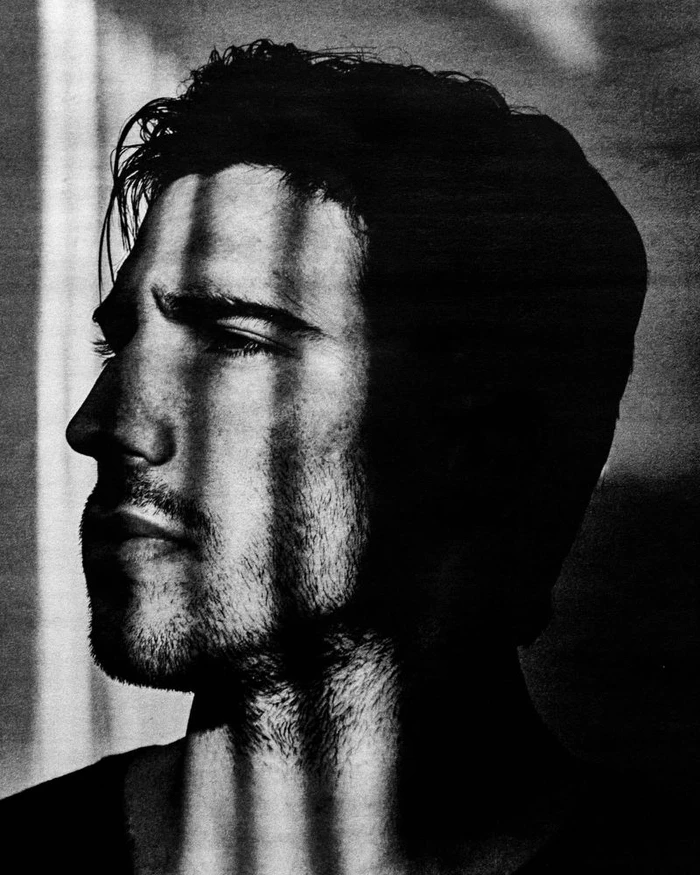 Close-up monochrome portrait of Sandro Tonali with heavy striped shadow casting across his face.