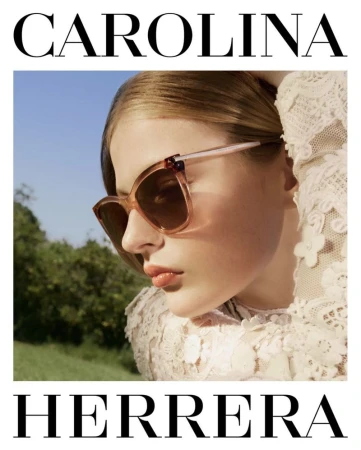 Close-up shot of a woman wearing sunglasses and a lace top outdoors under a blue sky, fashion advertisement for Carolina Herrera.
