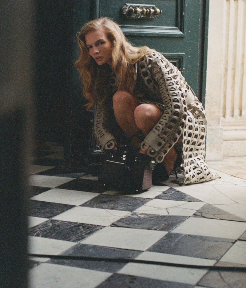 Model Caitlin Soetendal crouching in a patterned cutout coat on a checkered marble floor for D Repubblica Pause editorial