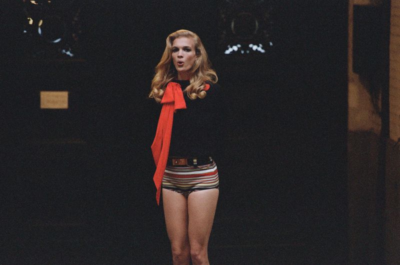Adult woman in retro-striped shorts and a black shirt with a red scarf, captured indoors with a dark background and studio lighting.