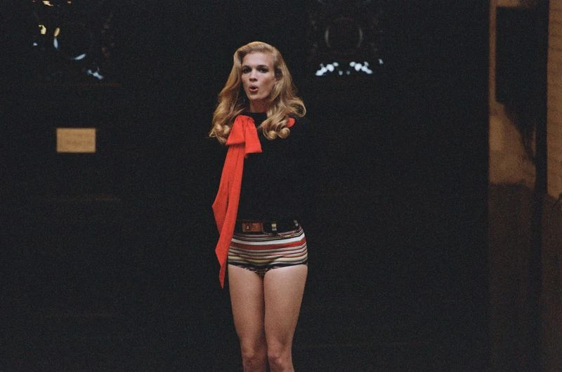 Adult woman in retro-striped shorts and a black shirt with a red scarf, captured indoors with a dark background and studio lighting.