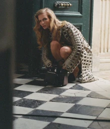Model Caitlin Soetendal crouching in a patterned cutout coat on a checkered marble floor for D Repubblica Pause editorial