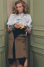 Model leaning against muted green double doors wearing a white blouse and layered brown skirt with colourful bangles