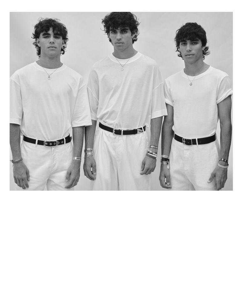 Black and white image of three adult males standing indoors wearing white shirts, white pants, and black belts, posing for a portrait.