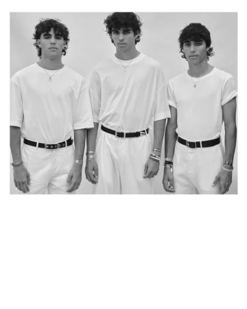 Black and white image of three adult males standing indoors wearing white shirts, white pants, and black belts, posing for a portrait.