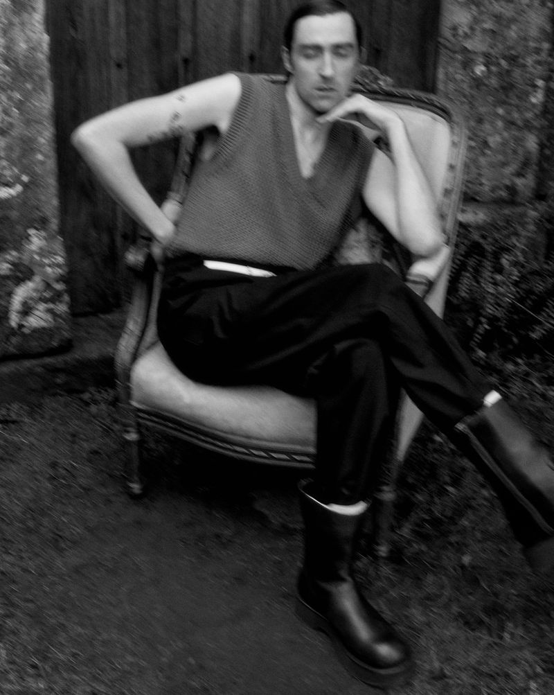 Monochrome portrait of a man seated in an ornate chair wearing a knit vest and dark trousers for U Repubblica.