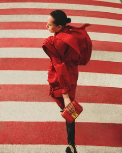 Model in a bright red outfit and carrying a red handbag walking across a striped red and white crosswalk