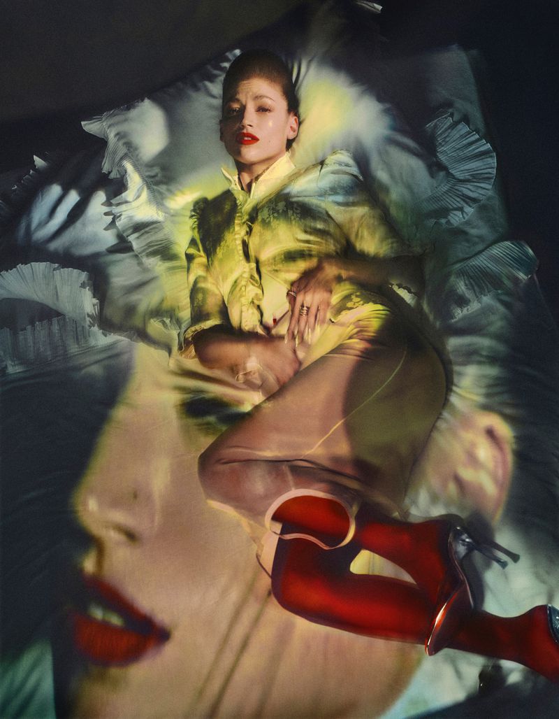 Overhead studio shot of a fashion model lying on a bed, red high heel boots on, and a face double exposure. Fashion and beauty editorial.