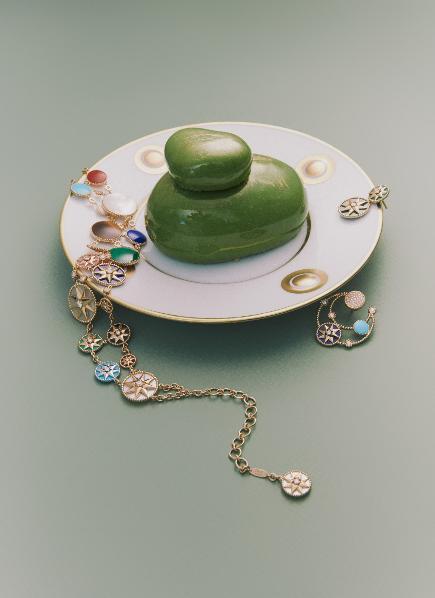 Elegant presentation of a green dessert on a decorative plate, complemented by gold jewelry on a light green surface.