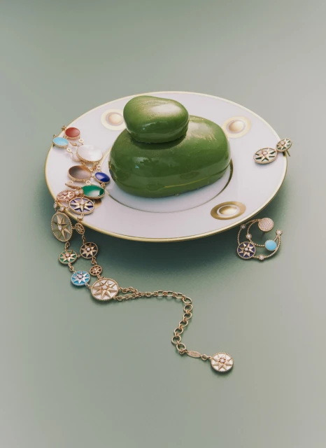 Elegant presentation of a green dessert on a decorative plate, complemented by gold jewelry on a light green surface.