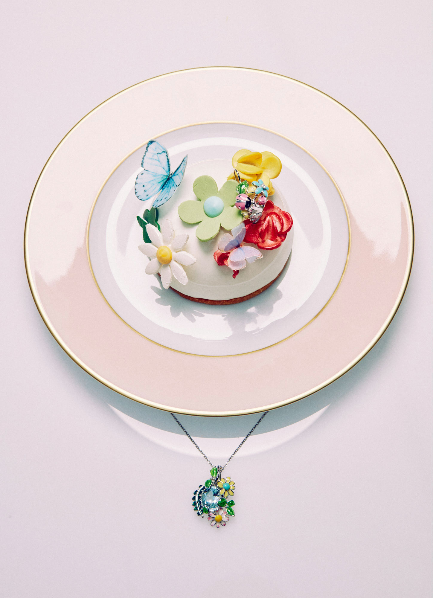 Overhead shot of a decorated dessert on a pink-trimmed plate with a colorful floral necklace against a white background.