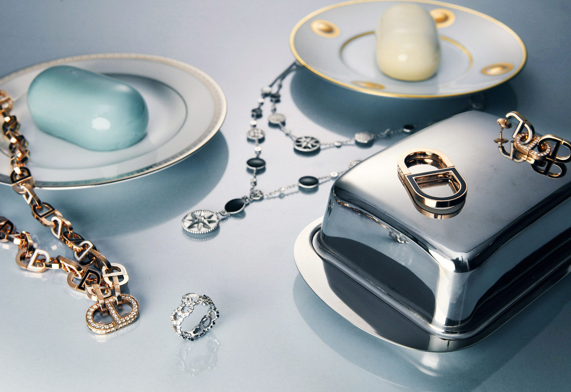 Still life shot of designer jewelry, soap, and metal serving dishes on a light gray surface creating an elegant and luxurious scene.