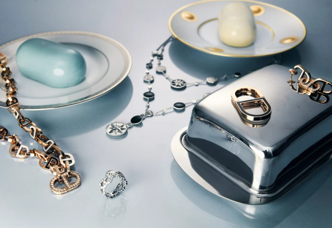 Still life shot of designer jewelry, soap, and metal serving dishes on a light gray surface creating an elegant and luxurious scene.