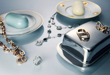Fine jewellery including gold necklaces, rings and silver pieces displayed alongside ceramic tableware on a reflective surface