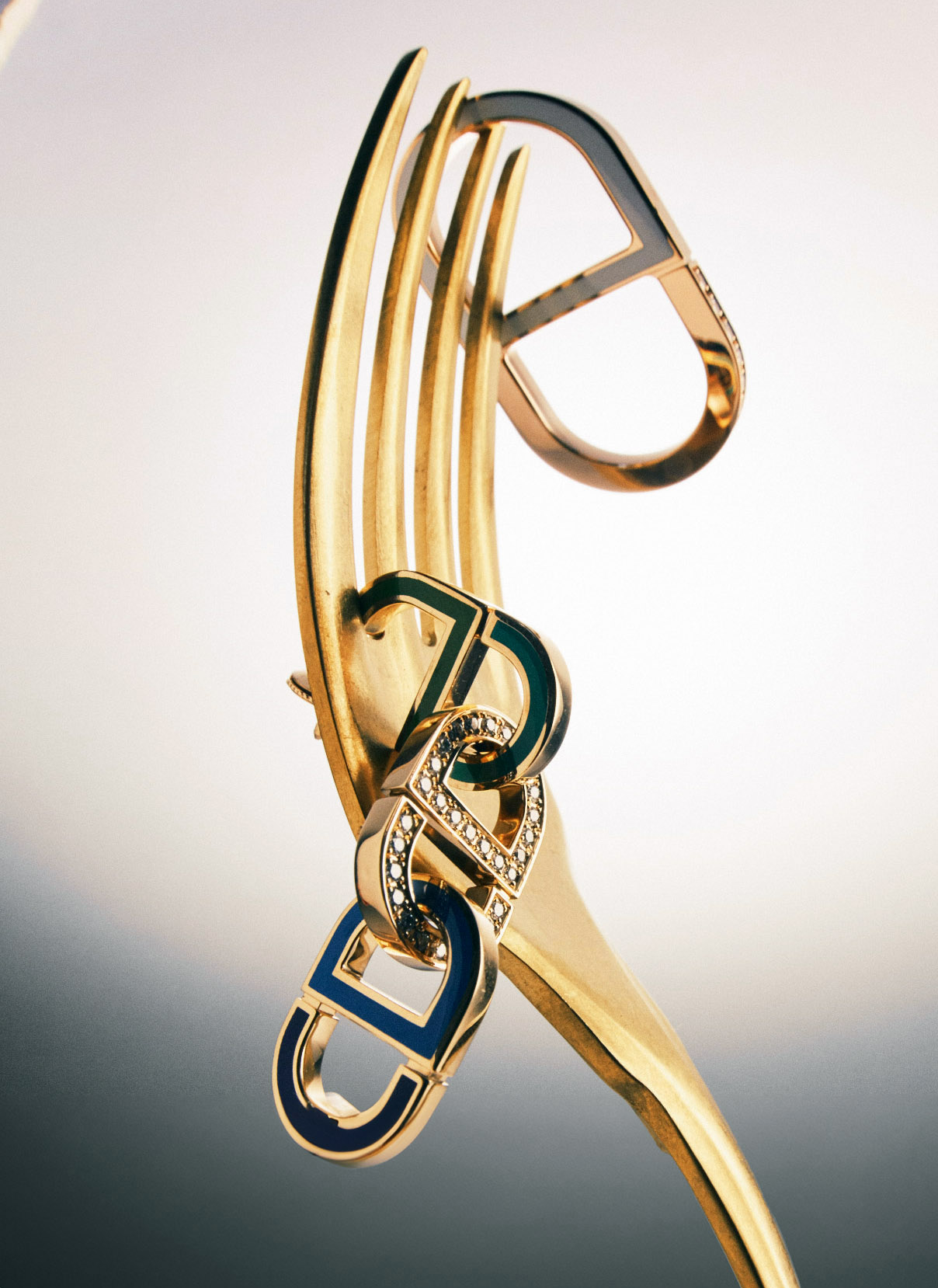 Gold fork with designer gold charm jewelry. The gold charms have diamonds and blue enamel. Studio shot with even lighting.