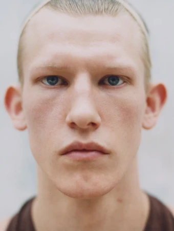 Close-up studio shot of an adult male with light complexion and blue eyes looking directly at the camera with a neutral expression.
