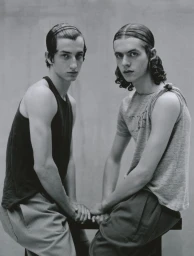 Two young male models sitting together wearing tank tops against a grey studio backdrop for Lampoon Magazine project Between us three.