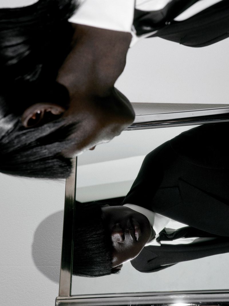 Black man in a black suit with a white shirt and black tie reflected in a vertical mirror