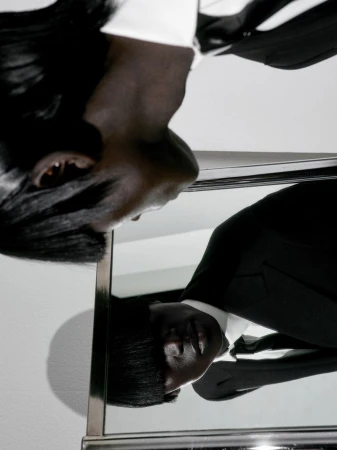 Black man in a black suit with a white shirt and black tie reflected in a vertical mirror