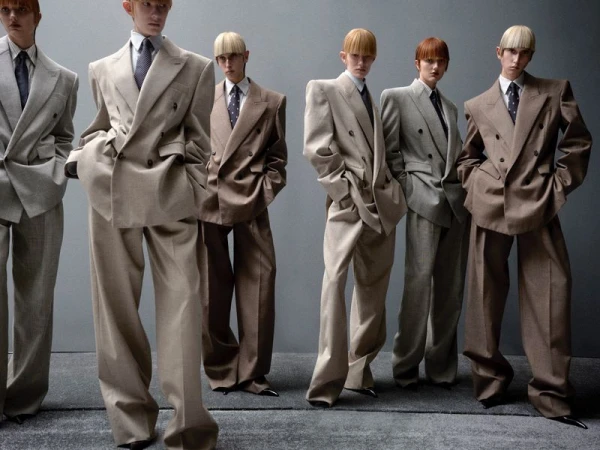 A group of androgynous fashion models wearing oversized suits posing in a studio with a gray backdrop, showcasing a modern, stylish aesthetic.