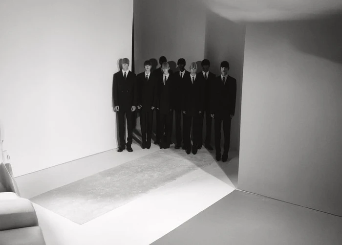 Group of models in dark suits standing in a minimalist white and grey studio space for Exhibition Magazine
