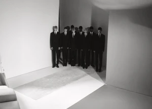 Group of models in dark suits standing in a minimalist white and grey studio space for Exhibition Magazine