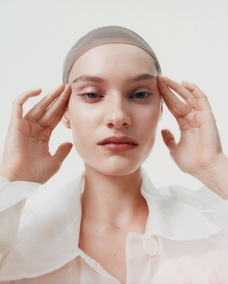 Close-up portrait of model Greta Hofer wearing a sheer cap and white collar against a seamless white background for British Vogue.