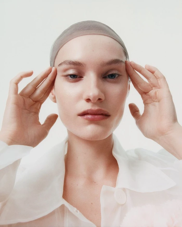 Close-up portrait of model Greta Hofer wearing a sheer cap and white collar against a seamless white background for British Vogue.