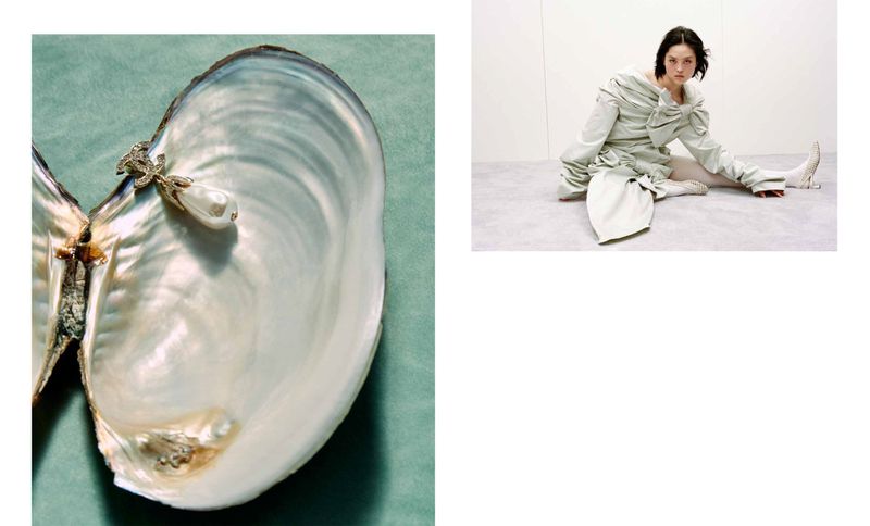 Fashion shot featuring a woman in an draped garment seated on the floor and a large open oyster shell on a green background.