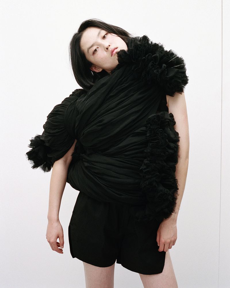 Model wearing sculptural black draped garment with ruffles against a plain white studio background for Nylon China