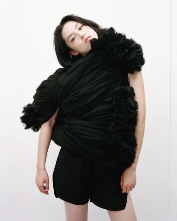 Model wearing sculptural black draped garment with ruffles against a plain white studio background for Nylon China