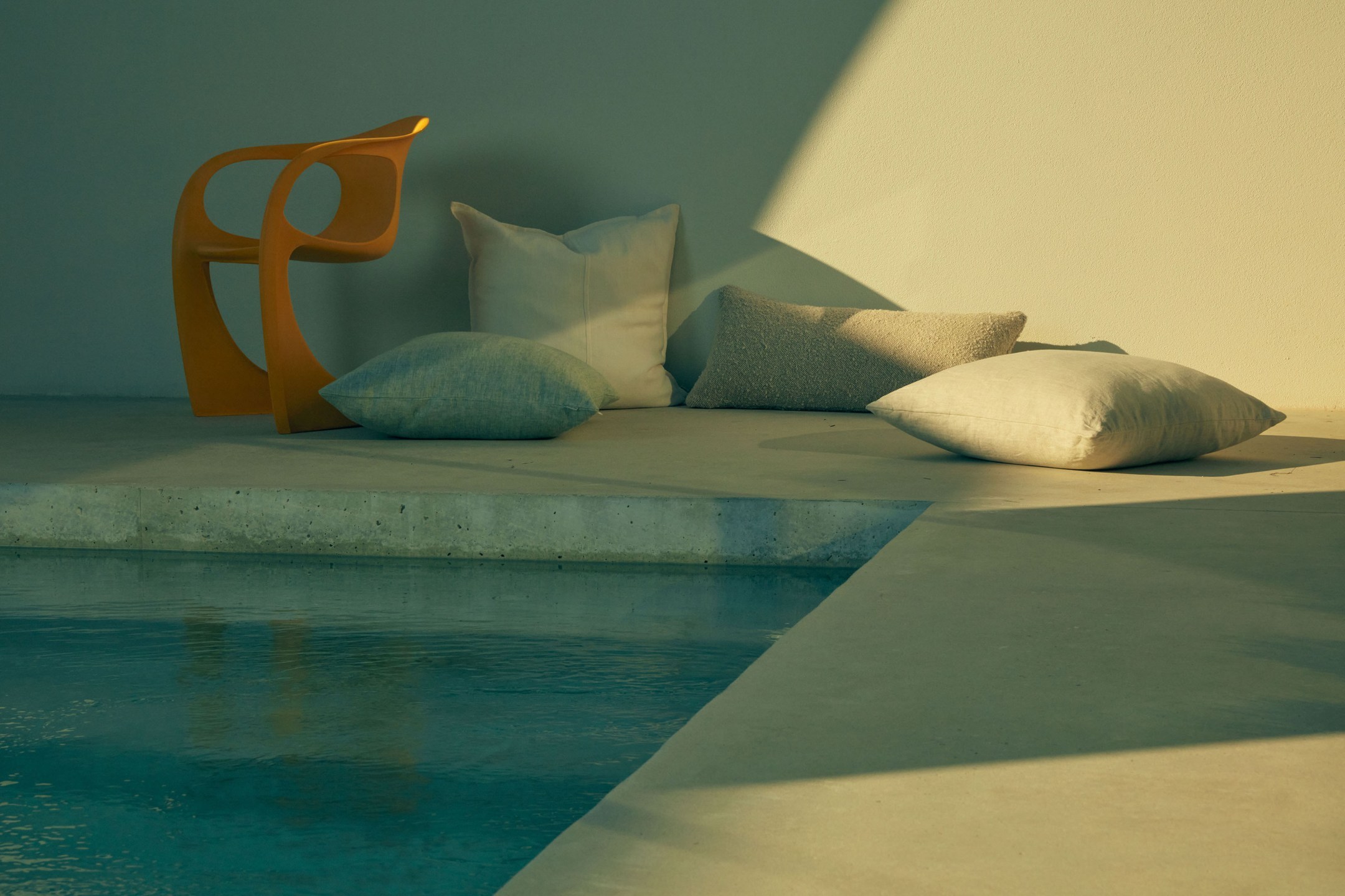 Modern yellow chair and several plush cushions arranged beside an outdoor pool under warm sunlight