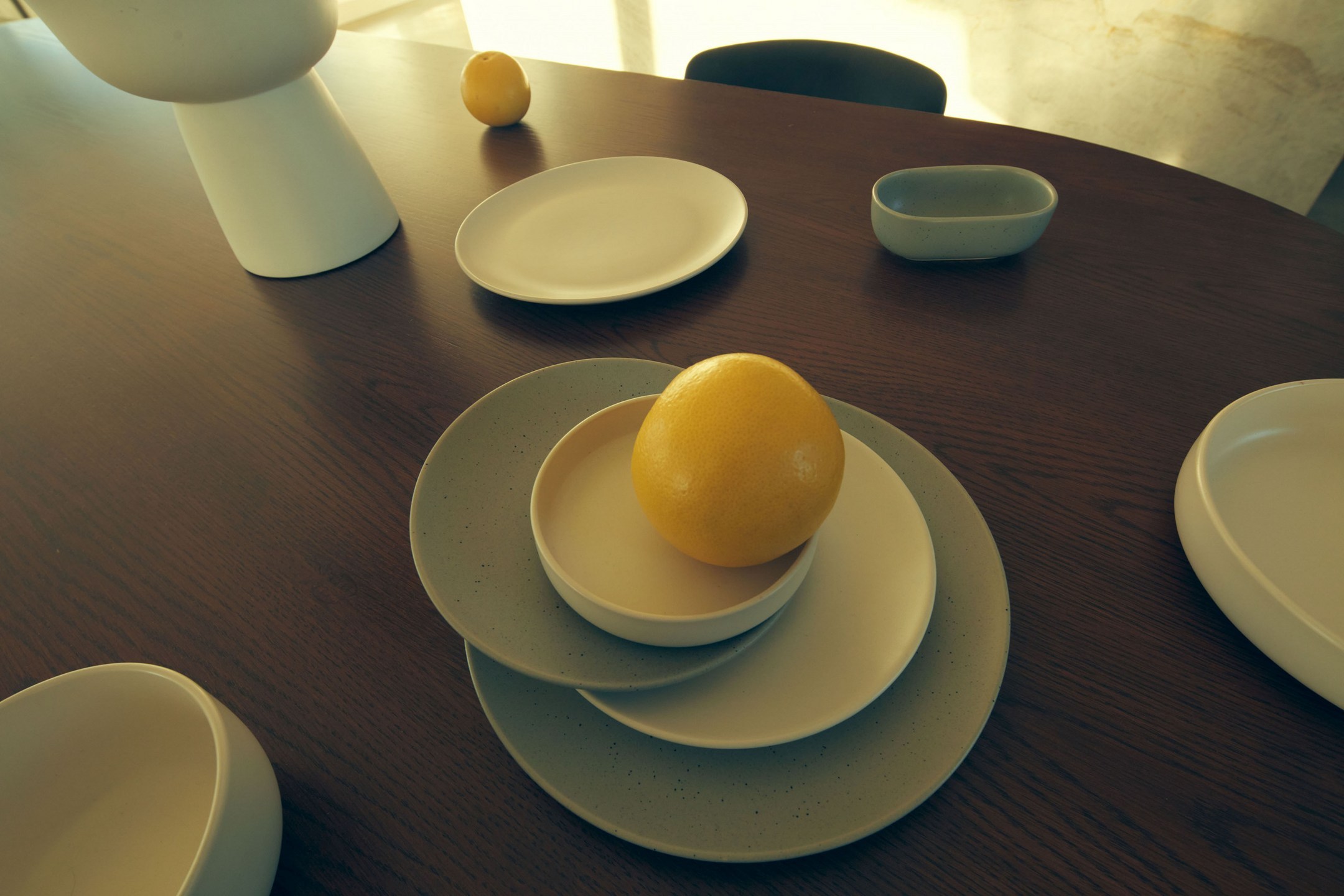 Overhead shot of a dark wood table setting with several white ceramic dishes, bowls, and a lemon centered on a plate.