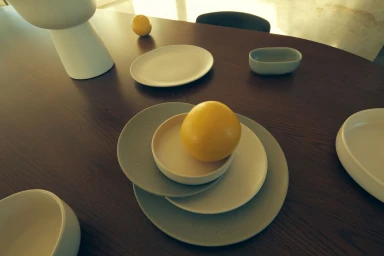 A bright yellow citrus fruit resting on stacked ceramic plates over a dark wooden tabletop surface.