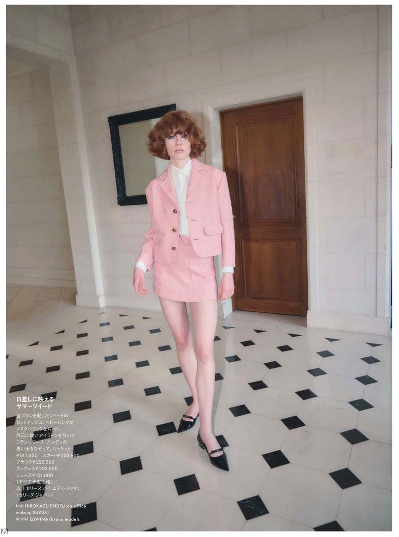 Fashion editorial shot of a woman in a pink skirt suit walking on a black-and-white checkered floor, with a door and artwork in the background.