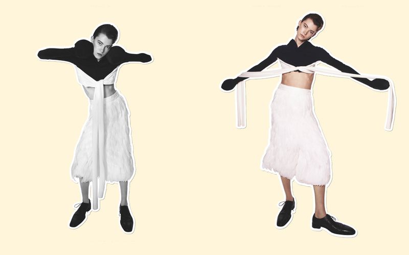 Two women pose in a studio wearing a black and white crop top with a skirt. The women strike a pose with their arms outstretched.