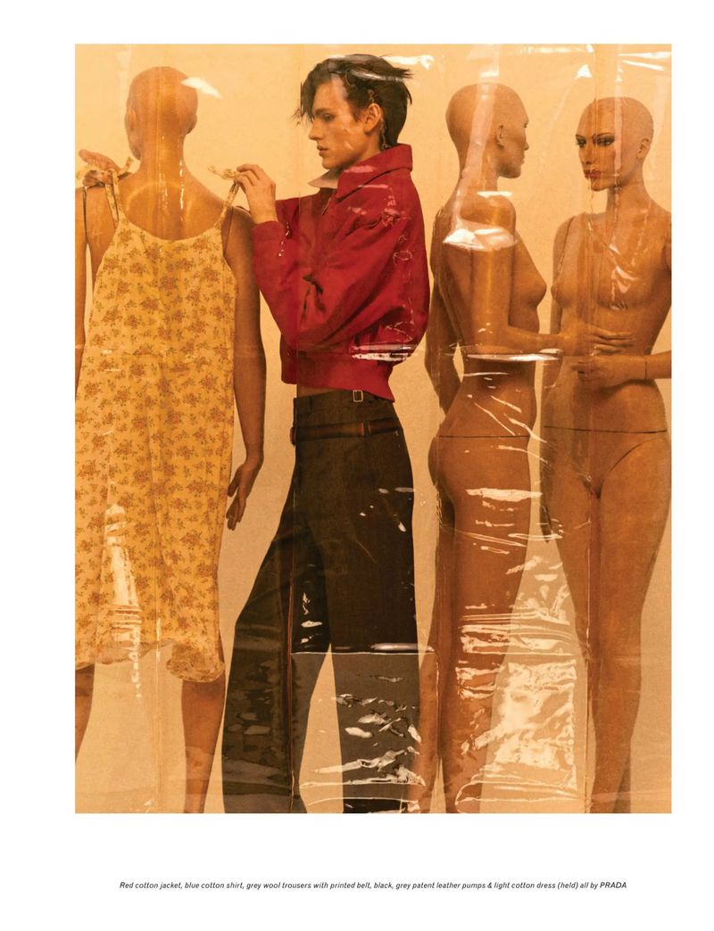 A person in a red jacket stands among several mannequins behind a plastic sheet for Pop Magazine.