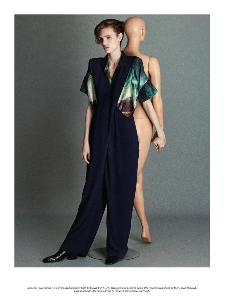 Fashion shot of a female model wearing a navy jumpsuit with printed top, standing next to a mannequin against a grey background.