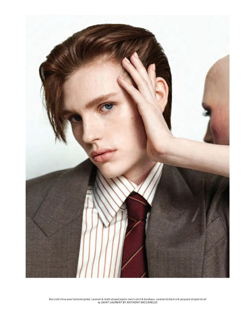 Close-up fashion shot of a young adult male model in a brown suit and striped shirt, with a second model's face partially visible.