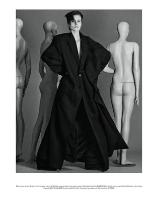 Model wearing an oversized black coat standing proudly among several mannequins in a studio setting for Pop Magazine