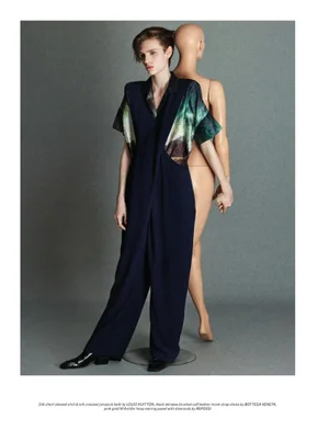 Model in dark jumpsuit standing beside a mannequin in a grey studio setting.