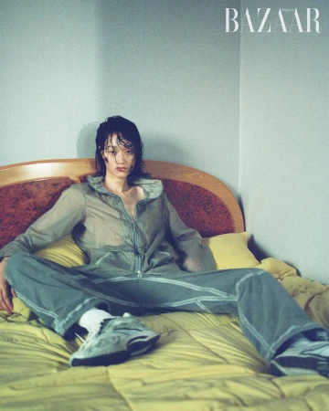 A person in a track suit sits cross-legged on a bed with a yellow quilt. The person is wearing sneakers and white socks. A magazine logo is visible.