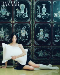 A model holding a white pillow while seated on the floor before a dark traditional cabinet with inlaid mother-of-pearl decorations.